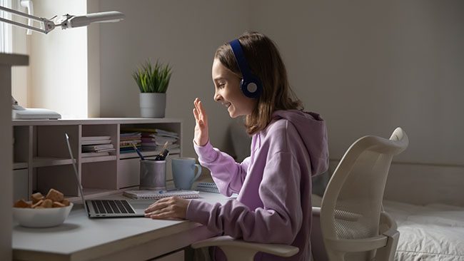 Smiling teenage girl have video call on laptop at home