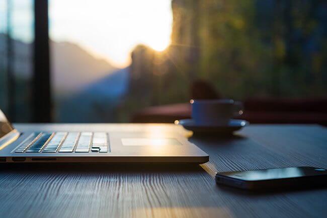 Computer Coffee Mug and Telephone on black wood table sun rising